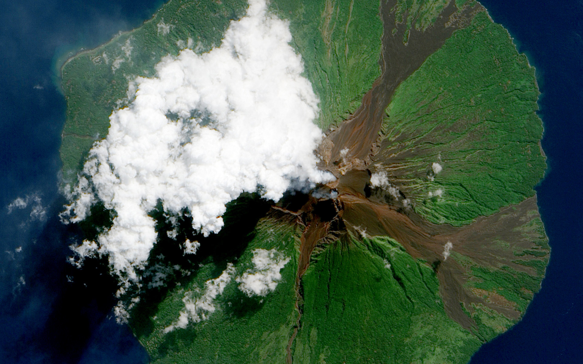 Вулкан Манам у побережья Папуа-Новой Гвинеи. Он образует остров диаметром в 10 км. Из кратера вулкана вырывается белый шлейф.
